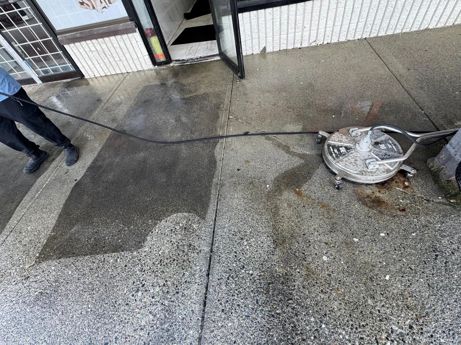 A Deoro crew member running a rotary surface cleaner along a commercial walkway, the treated concrete visibly lighter than the untreated section.